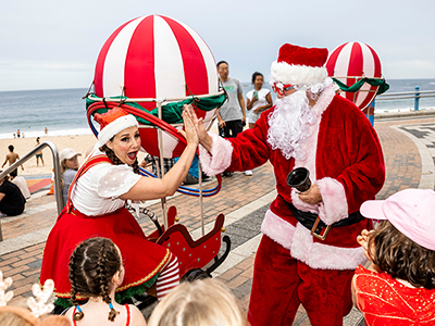 A photo of Santa and an elf high-fiving at Coogee Beach.