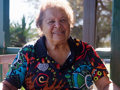 A photograph of Aunty Marjorie Dixon, sitting in the sunshine, laughing