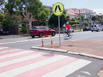 The busy intersection on Maroubra Road, with a car and a pedestrian walking past