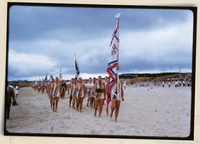 1959 photograph of members of the Maroubra Surf Lifesaving Club parading on the beach with flags
