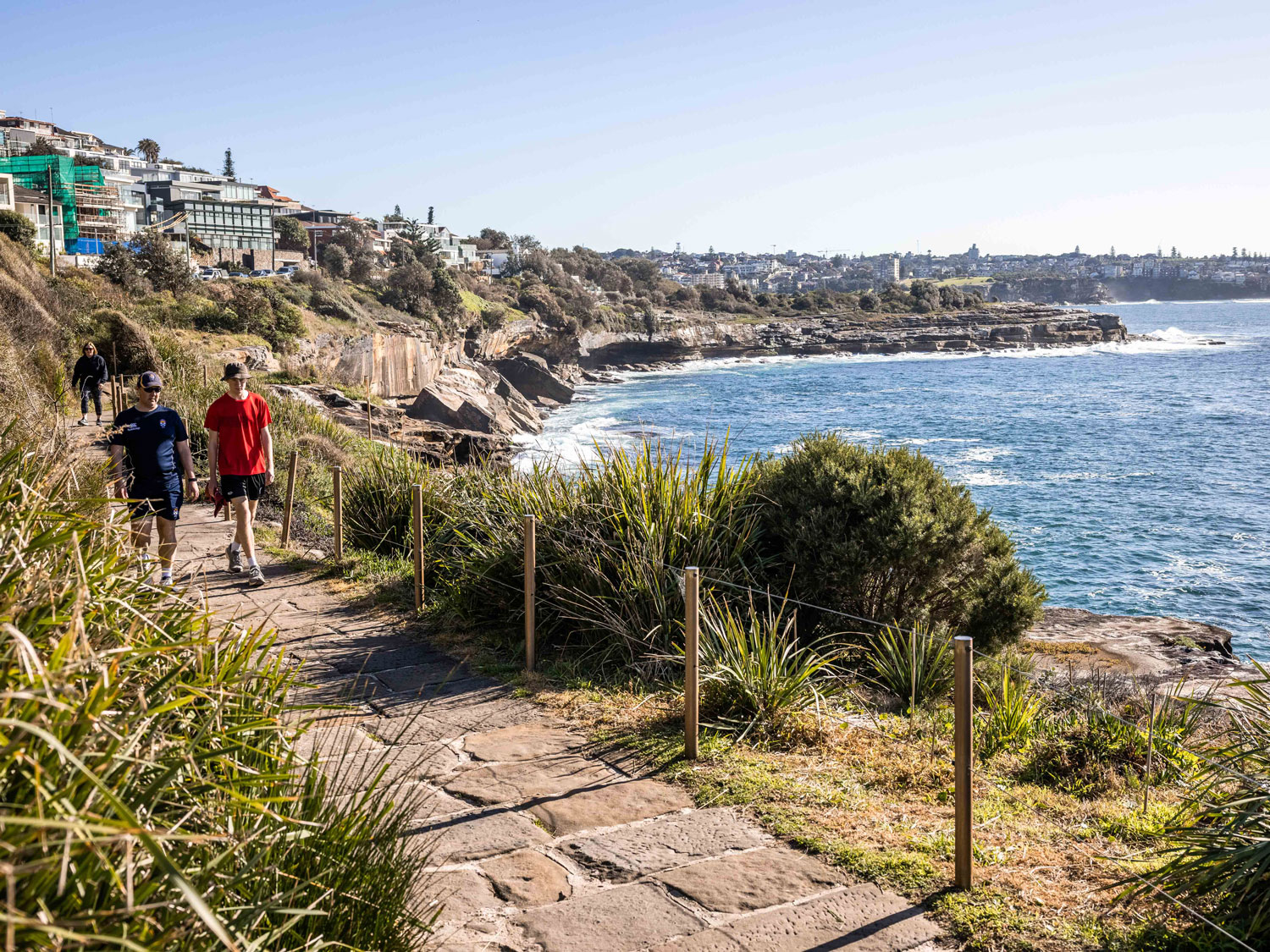 A photo of two people walking along the coastline.