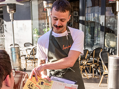 A waiter presenting a menu at Maybe Frank in Randwick, in the alfresco dining area