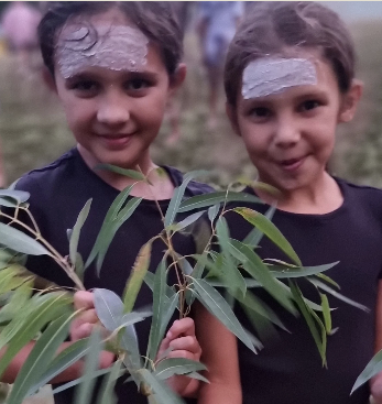Two young girls with chalk face paint, holding some eucalyptus leaves up to camera