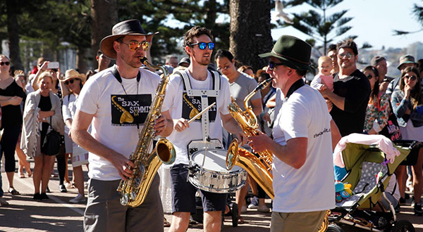 3 musicians playing saxophone and drums at Coogee beach in front of crowd