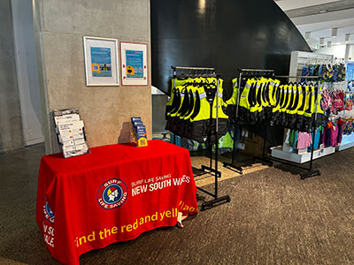A photograph of a life jacket library sitting next to a table on which the red tablecloth of the Surf Life Saving organisation has been laid out.