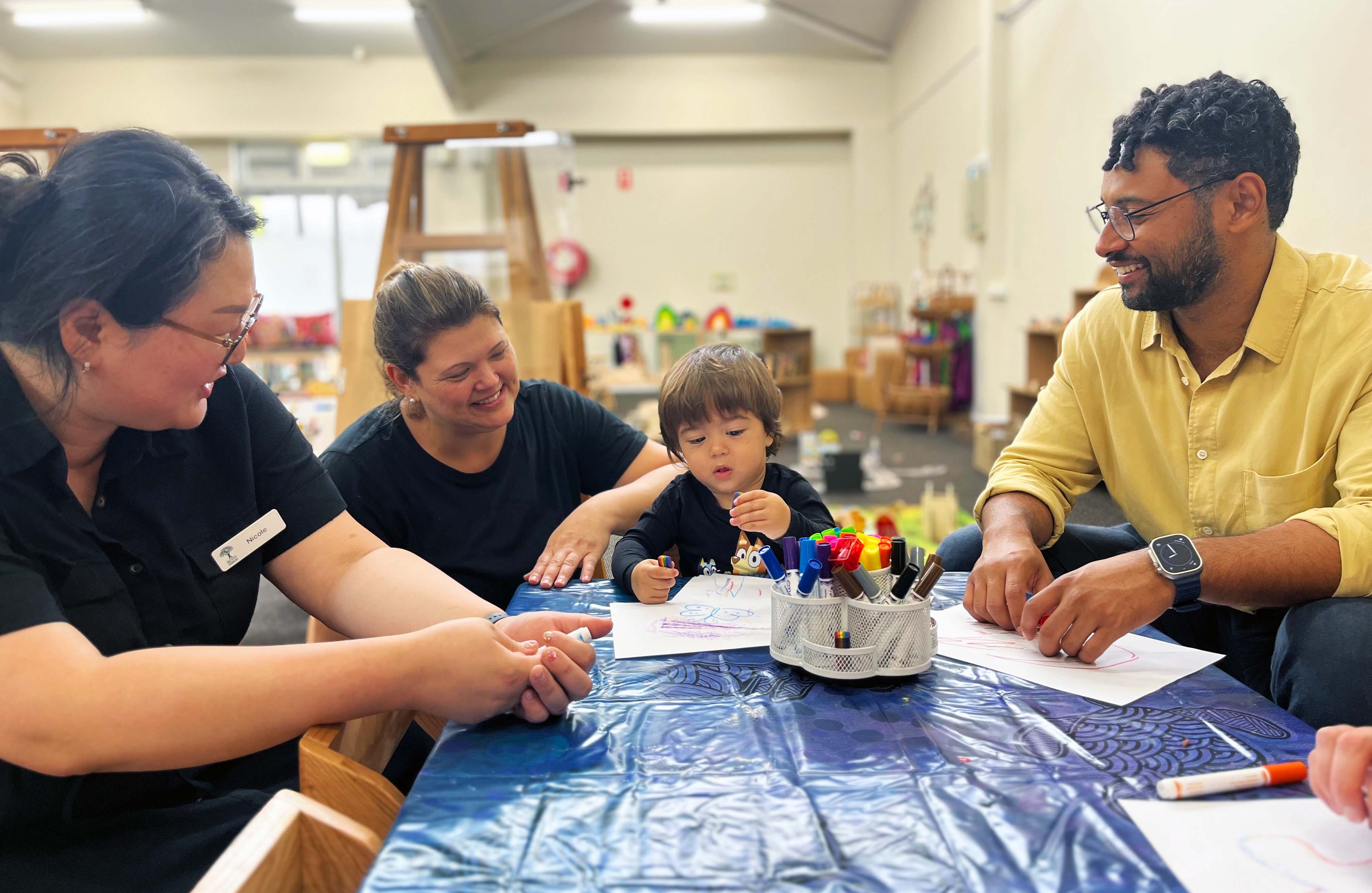 Max and 21 of his classmates returned to childcare this week at the temporary facility. A photo of three adults including Randwick Mayor Dylan Parker watching a young boy draw.