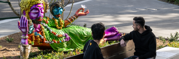 A colourful brone statue reclines in front of two people who are sitting. 