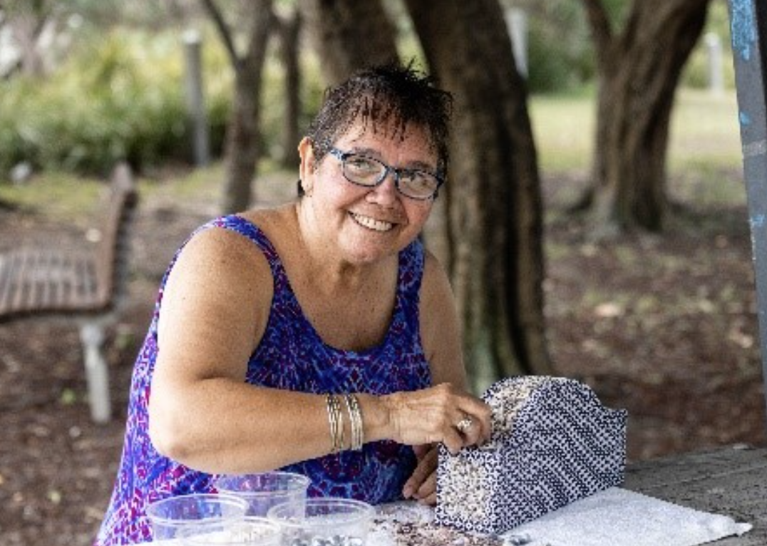 A woman smiles at camera whilst creating shell art