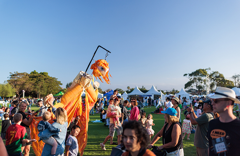 An image of a big roaming puppet among a crowd at a festival.