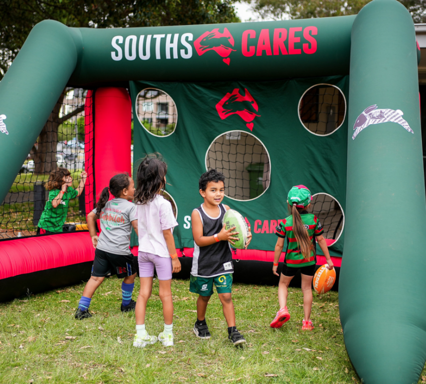 Children playing with a large inflatable target for football throwing practices, emblazened with the Rabbitohs logo